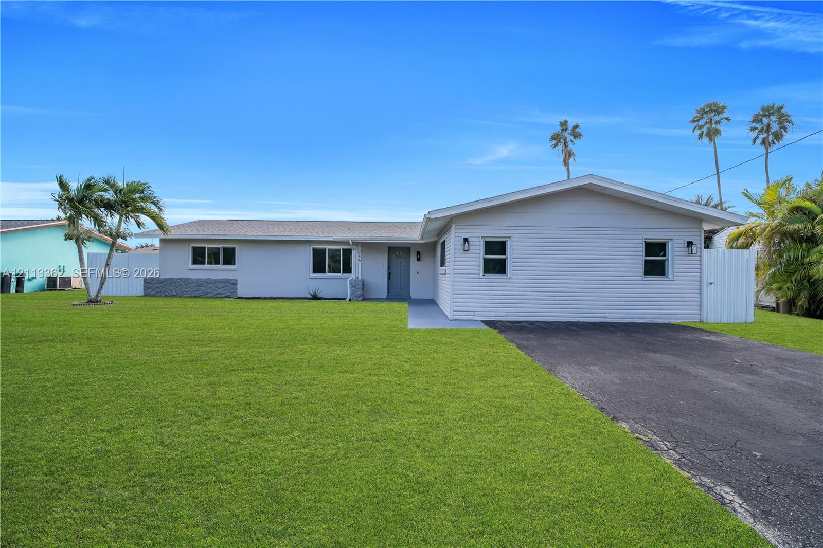 Single-story residence featuring light-colored horizontal siding, a pitched shingle roof, paved driveway, and expansive lawn Single-story residence featuring light-colored horizontal siding, a pitched shingle roof, paved driveway, and expansive lawn