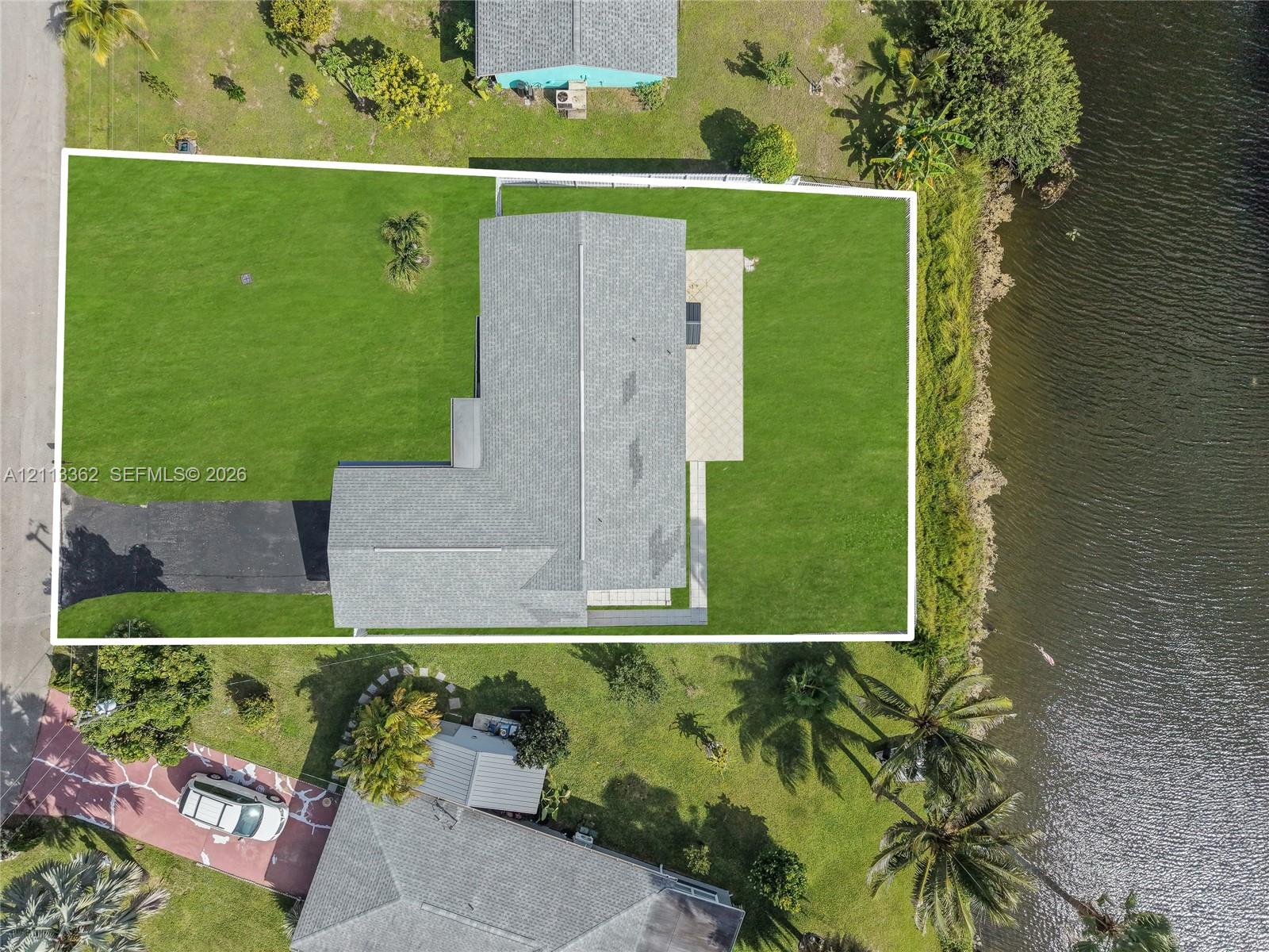 Aerial perspective featuring a waterfront lot, asphalt driveway, asphalt shingle roofing, and paved patio area