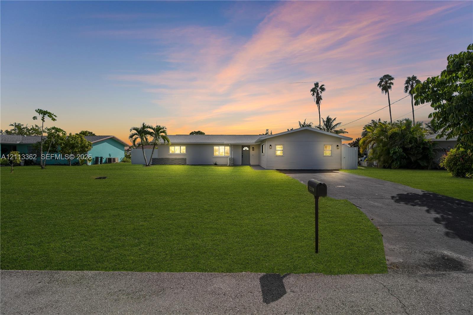 Single-story exterior featuring light-toned siding, a multi-gabled roofline, an expansive front lawn, and a paved driveway Single-story exterior featuring light-toned siding, a multi-gabled roofline, an expansive front lawn, and a paved driveway