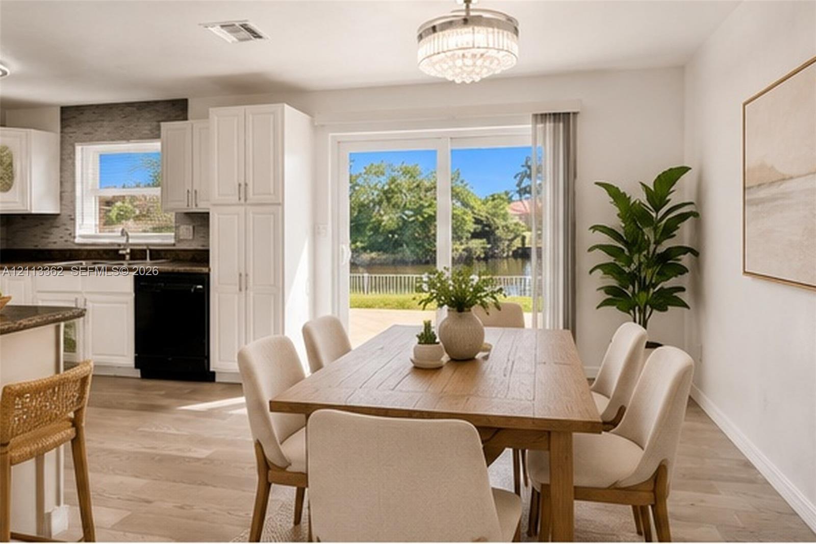Kitchen featuring white shaker-style cabinetry, a textured tile backsplash, and wood-finish flooring, with sliding glass doors opening to a waterfront exterior Kitchen featuring white shaker-style cabinetry, a textured tile backsplash, and wood-finish flooring, with sliding glass doors opening to a waterfront exterior