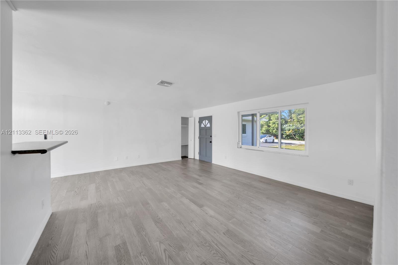 Open-concept interior featuring wood-finish flooring, neutral walls, a breakfast bar, and a multi-pane window