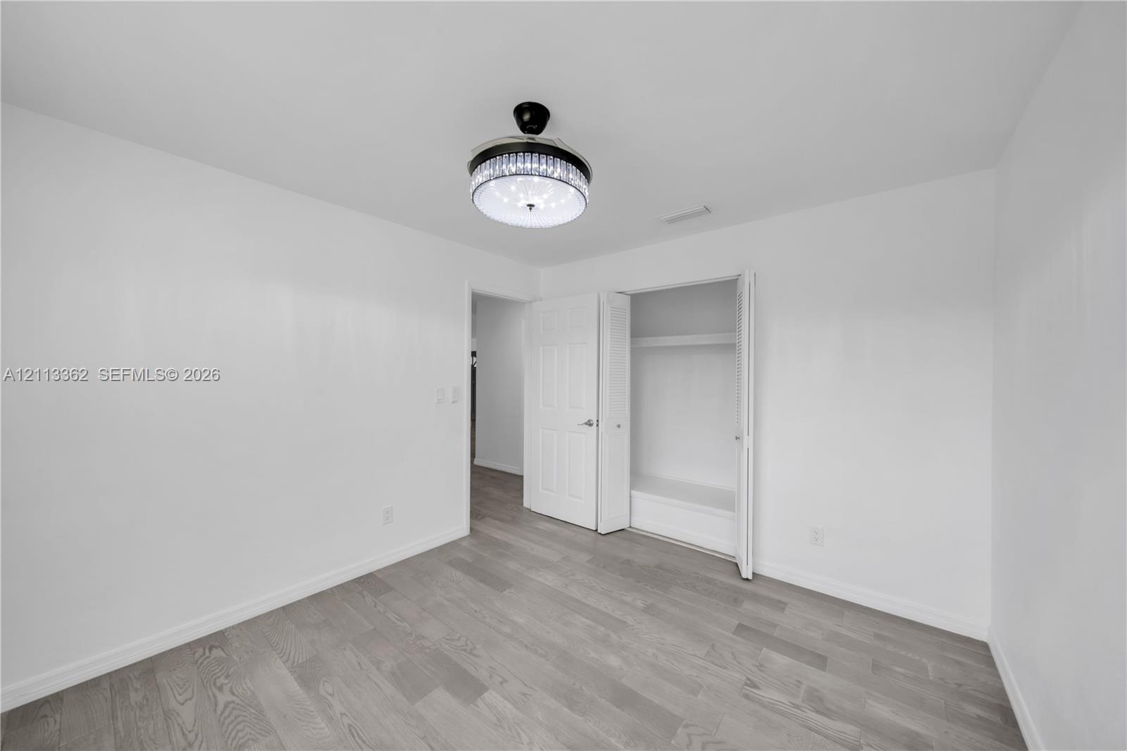 Wood-finish flooring, crystal-accented flush mount ceiling light fixture, and closet with built-in shelving