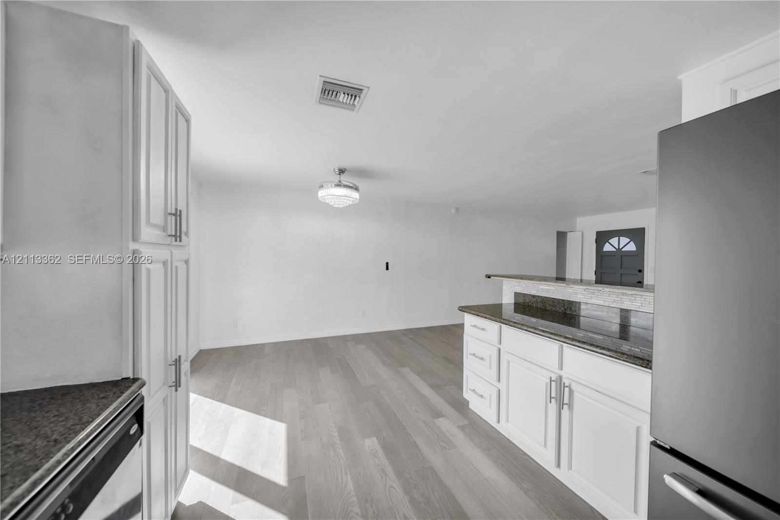 Kitchen featuring white shaker-style cabinetry, dark stone-finish countertops, wood-finish flooring, and a crystal-accented flush-mount light fixture