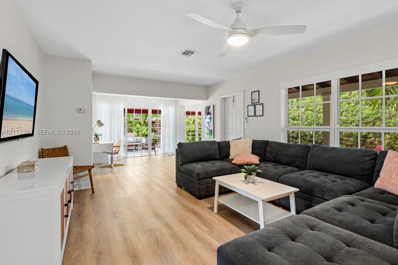 Living area featuring wood-finish flooring, a ceiling fan with integrated lighting, multi-pane windows, and sliding glass doors
