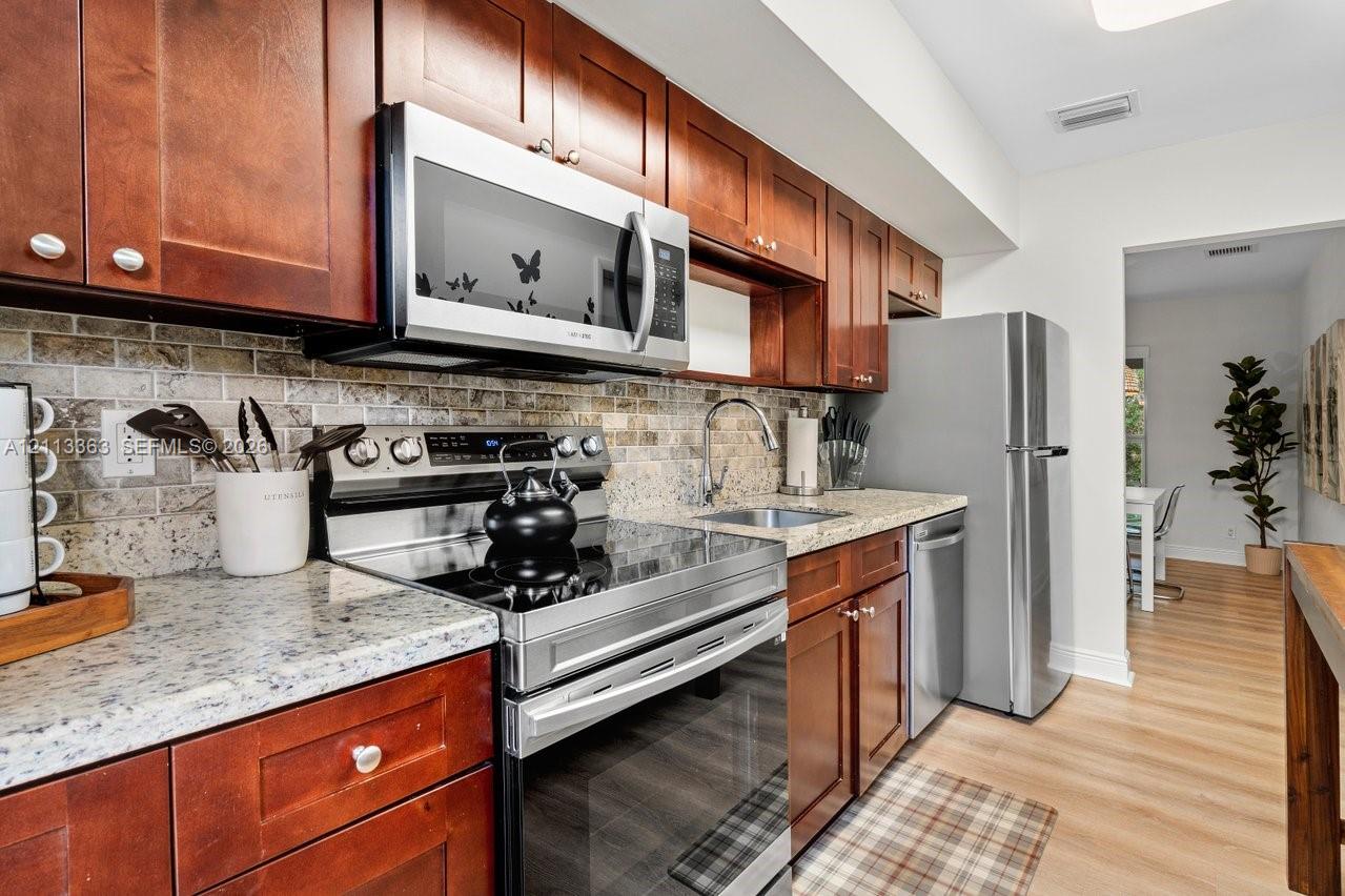 Kitchen featuring stained wood cabinetry, stone-finish countertops, stainless steel appliances, and a tiled backsplash