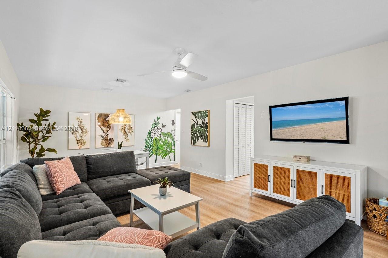 Living area featuring light-toned wood-finish flooring, a white ceiling fan with integrated lighting, and a white bi-fold closet door