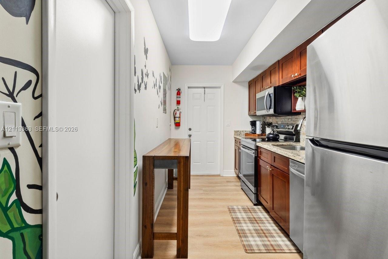 Galley-style kitchen featuring wood cabinetry, stone-finish countertops, stainless steel appliances, and wood-finish flooring