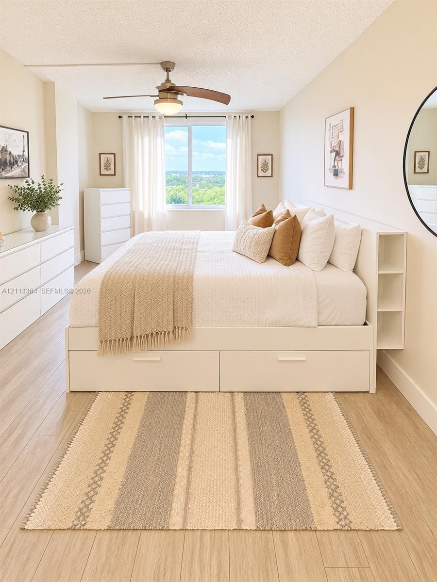 Wood-finish flooring, ceiling fan with integrated lighting, and large window with exterior tree-lined backdrop