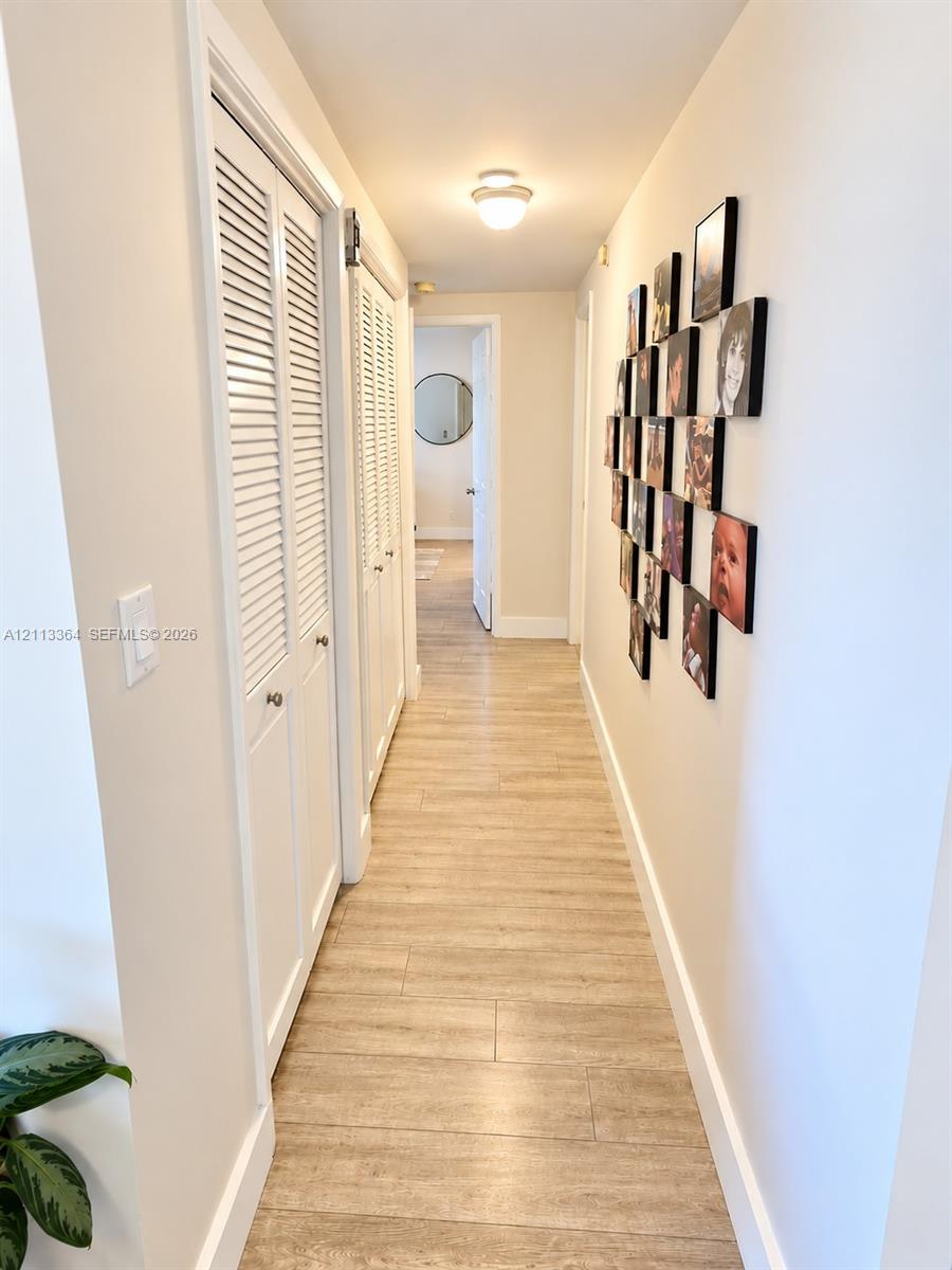 Hallway featuring wood-finish tile flooring, white louvered closet doors, and a flush-mount ceiling light fixture
