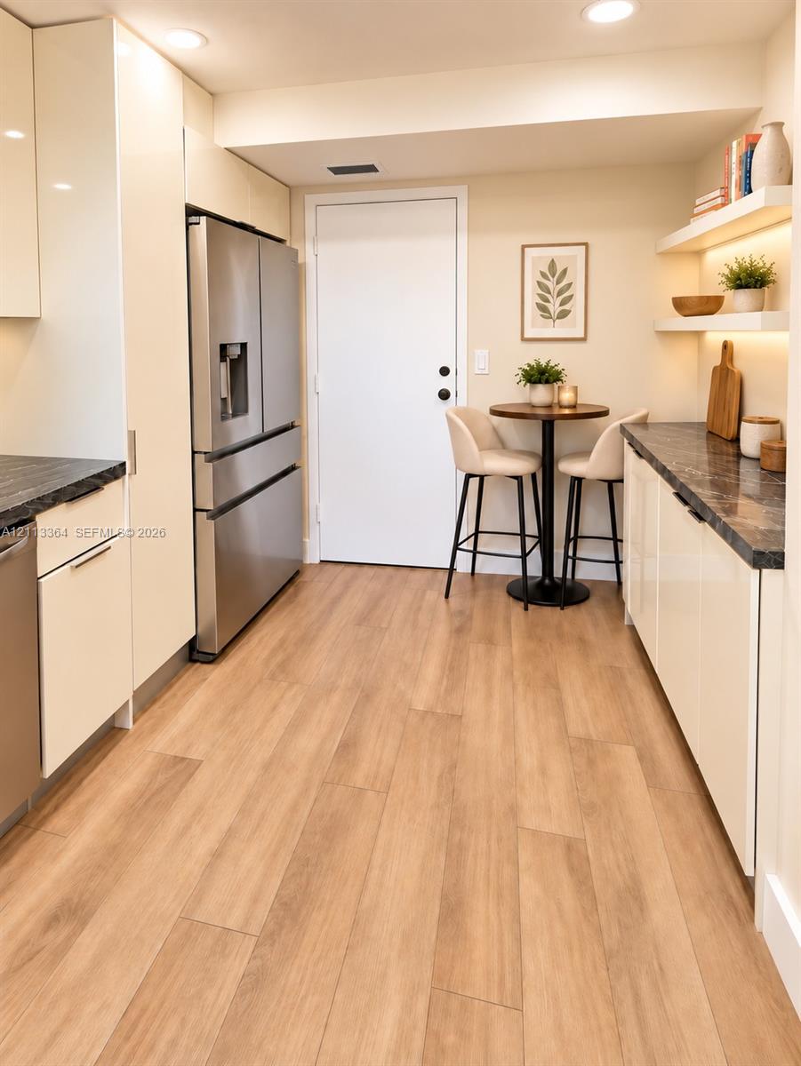 Kitchen featuring high-gloss cabinetry, stone-finish countertops, stainless steel appliances, integrated under-shelf lighting, and wood-finish flooring