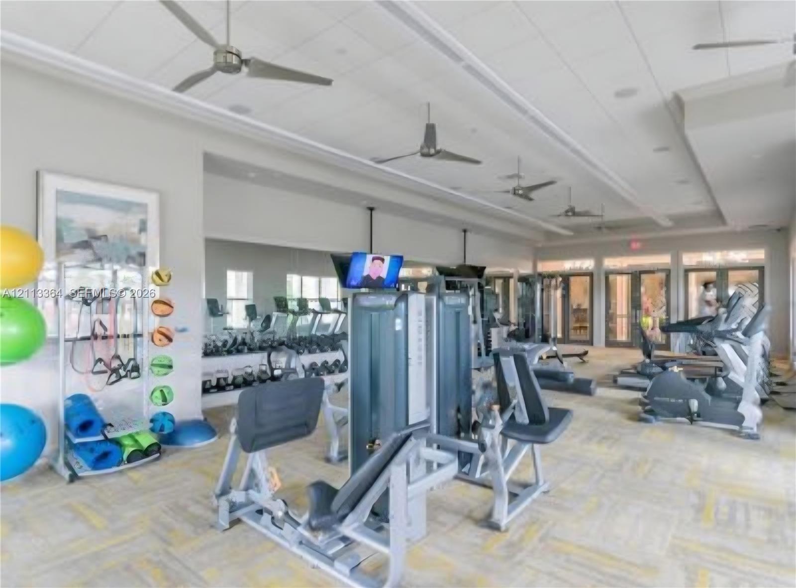 Fitness area featuring full-wall mirrors, recessed lighting, industrial ceiling fans, and glass-paneled double doors