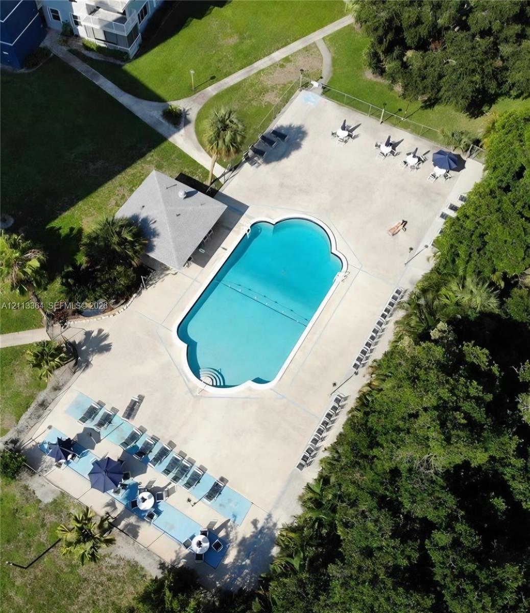 Swimming pool with a custom-shaped basin, surrounding concrete deck, covered cabana structure, and landscaped perimeter