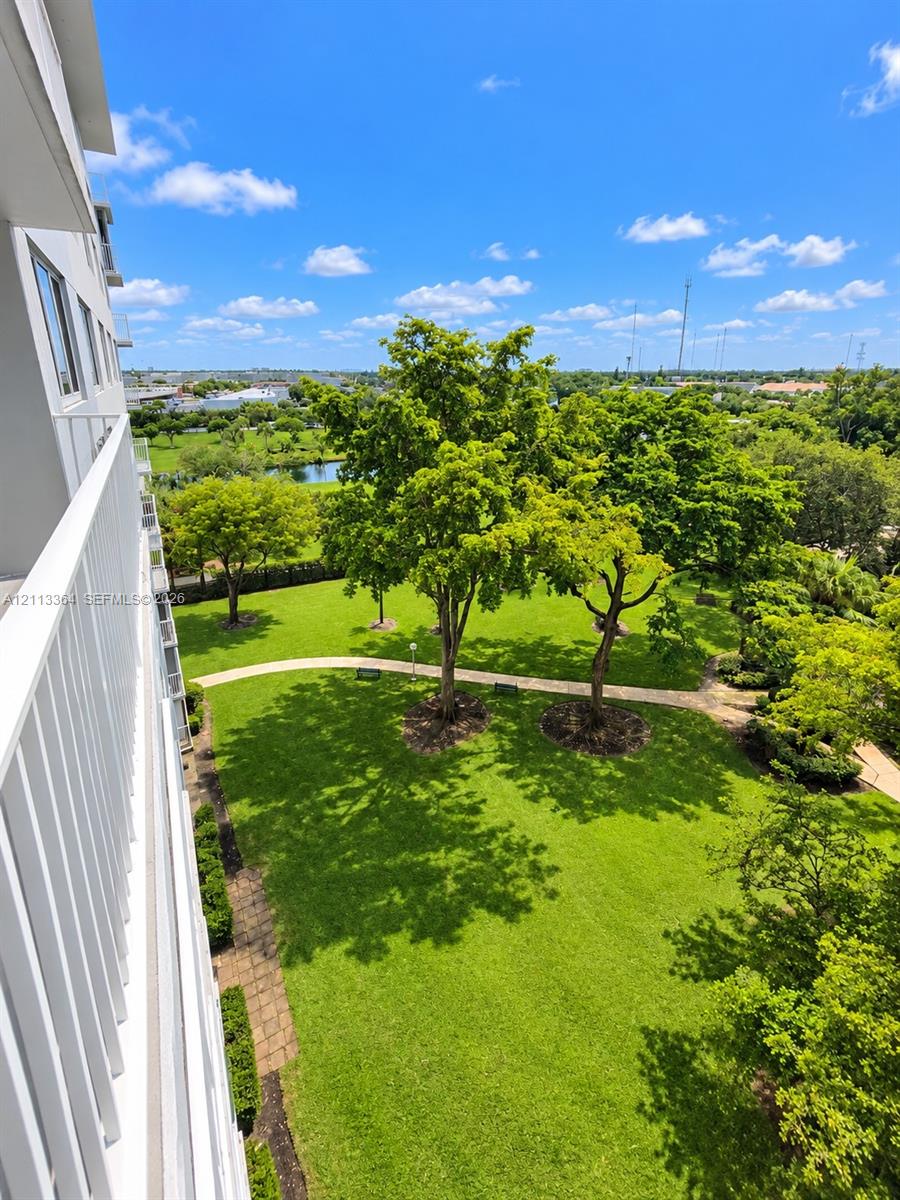 Elevated exterior balcony featuring white metal railing overlooking landscaped grounds with mature trees, expansive lawns, and stone-paved walkways