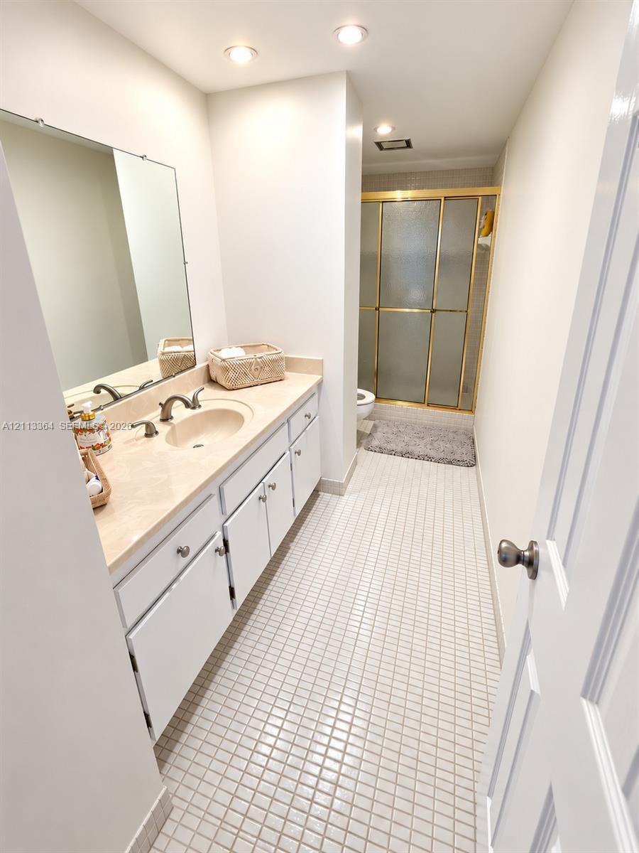 Bathroom featuring a white vanity with integrated basin, solid surface countertop, wall-to-wall mirror, tiled flooring, and a walk-in shower enclosure