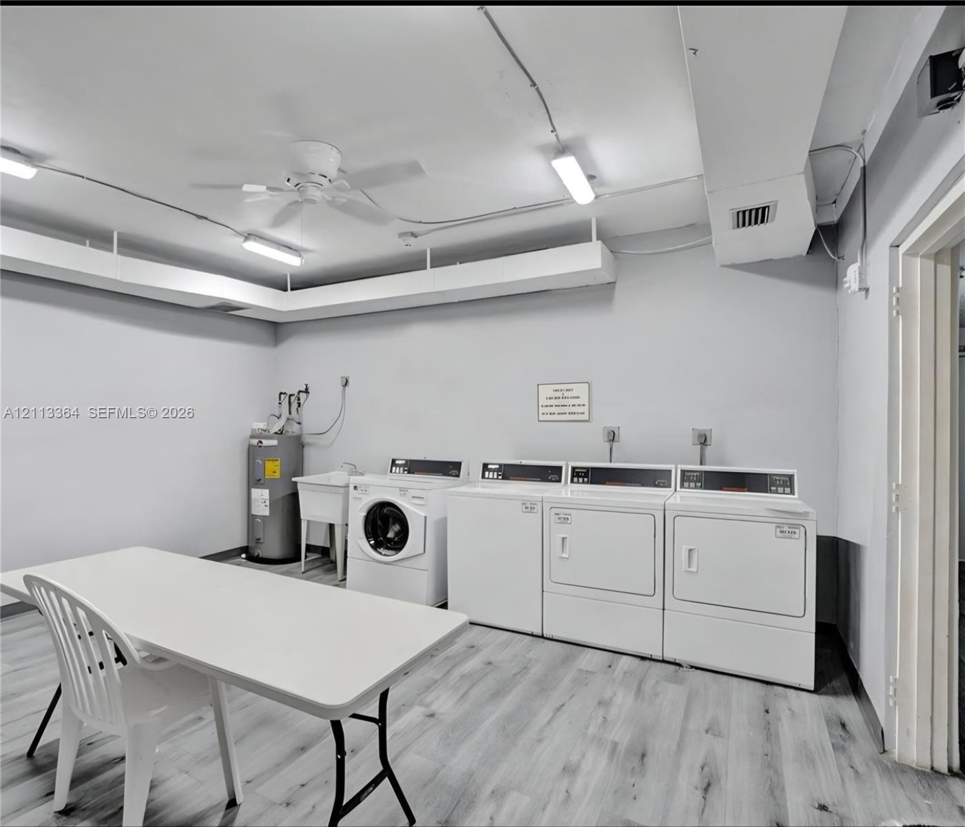Utility room featuring wood-finish flooring, a porcelain utility sink, and multiple built-in laundry appliances