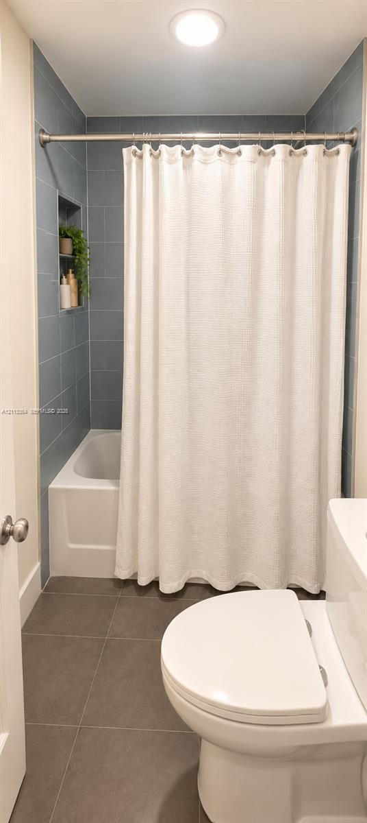 Bathroom featuring a tub-shower combination with blue tile surround, an integrated wall niche, large-format grey floor tile, and a flush-mount ceiling light