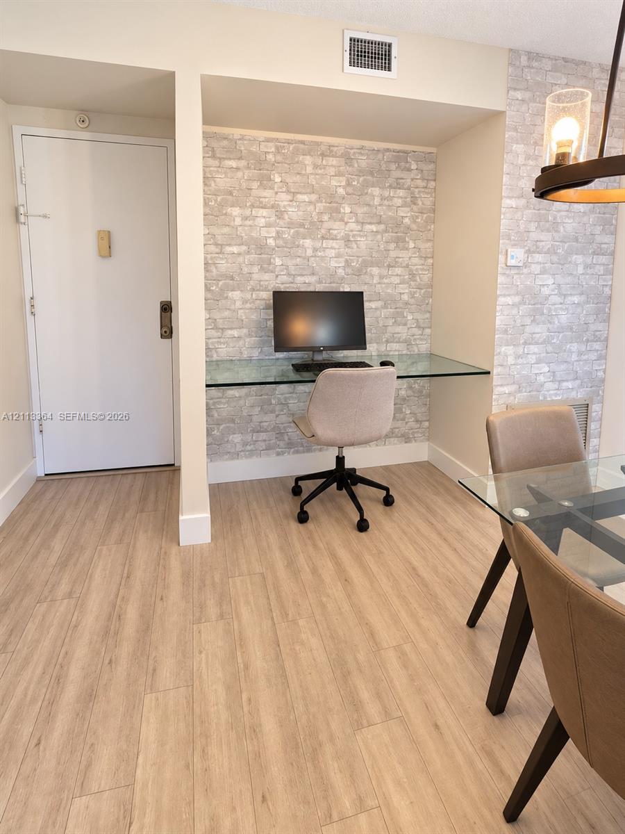 Built-in desk alcove with glass desktop and faux-brick wall accent, wood-finish flooring, and pendant lighting