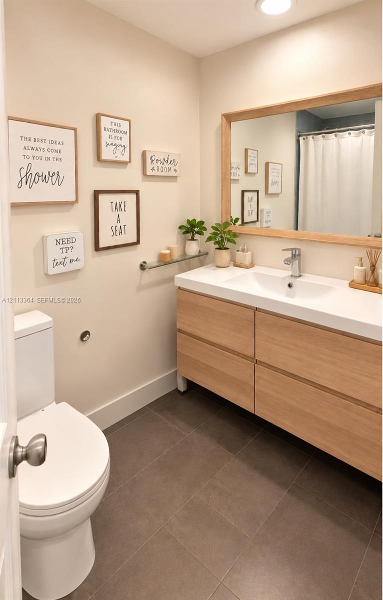 Bathroom featuring a wood-finish floating vanity with a rectangular integrated sink, large wood-framed mirror, chrome faucet, and tile flooring