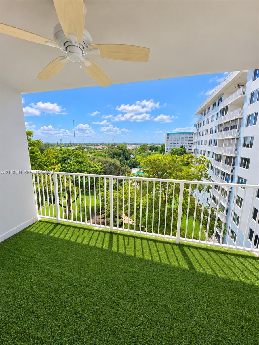 Covered balcony featuring synthetic turf flooring, a white metal railing, and a ceiling-mounted paddle fan