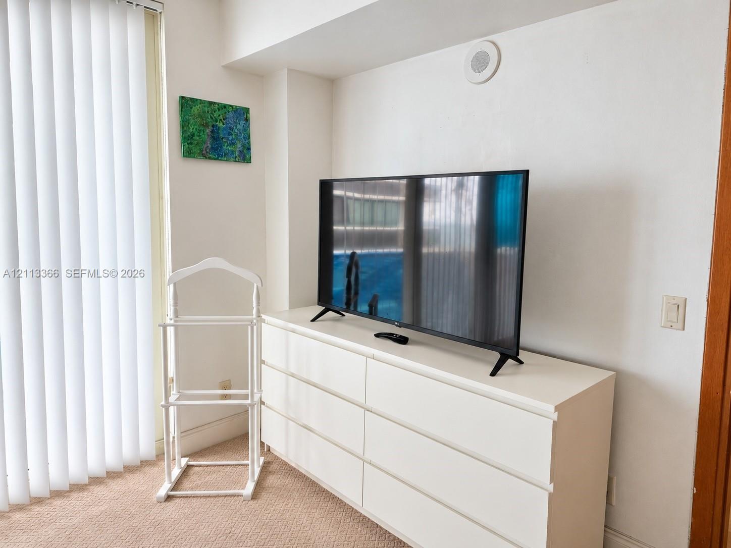 Neutral-toned carpeting, floor-to-ceiling vertical blinds, and recessed ceiling speaker