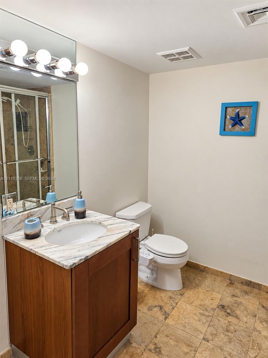 Bathroom featuring a vanity with a light-veined countertop and an oval undermount sink, large wall-mounted mirror, brushed metal fixtures, and stone tile flooring