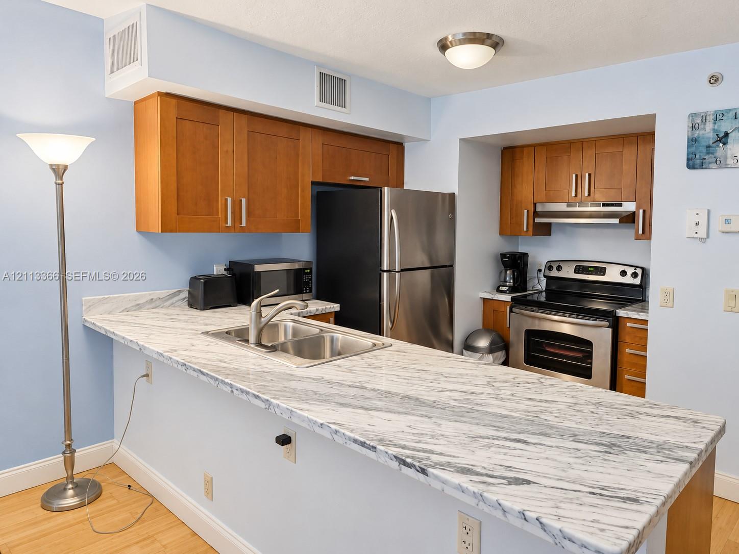 Kitchen featuring wood-finish cabinetry, stone-patterned countertops, a stainless steel double-basin sink, and integrated stainless steel appliances Kitchen featuring wood-finish cabinetry, stone-patterned countertops, a stainless steel double-basin sink, and integrated stainless steel appliances