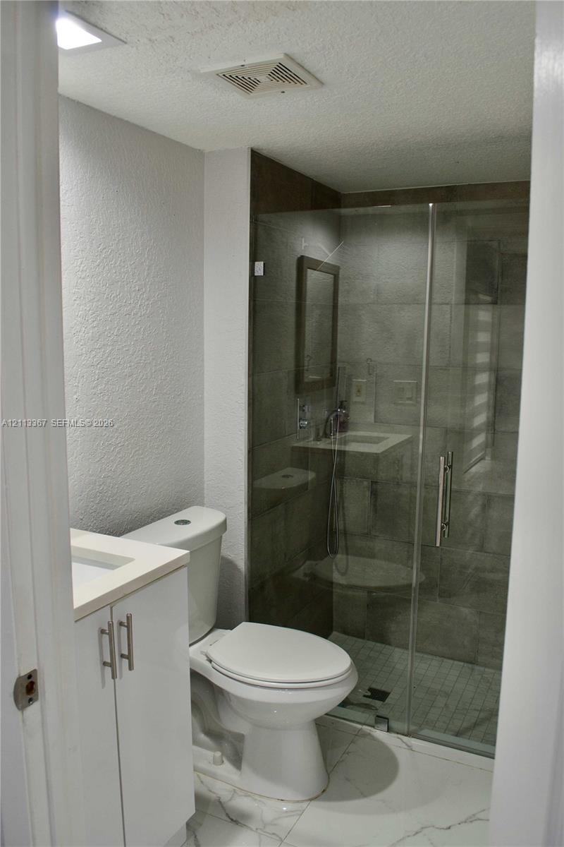 Bathroom featuring large-format tile flooring, white cabinetry with a light-toned countertop, and a walk-in shower enclosed by a glass door with tiled wall surrounds