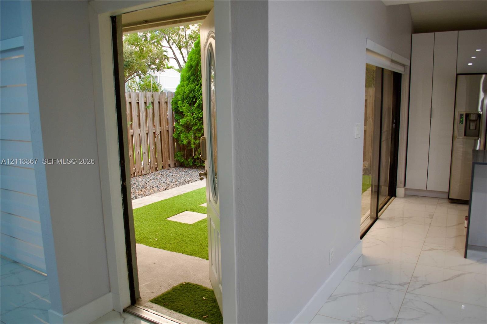 Large-format tile flooring, white floor-to-ceiling cabinetry, sliding glass door, and exterior access to a fenced courtyard featuring synthetic turf and stone pavers