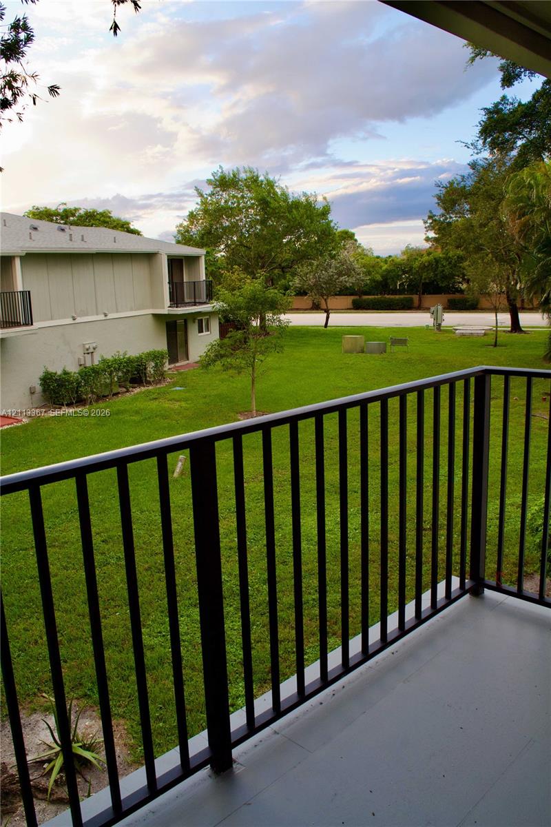 Private balcony featuring a black metal railing and concrete flooring, overlooking an expansive lawn with mature trees