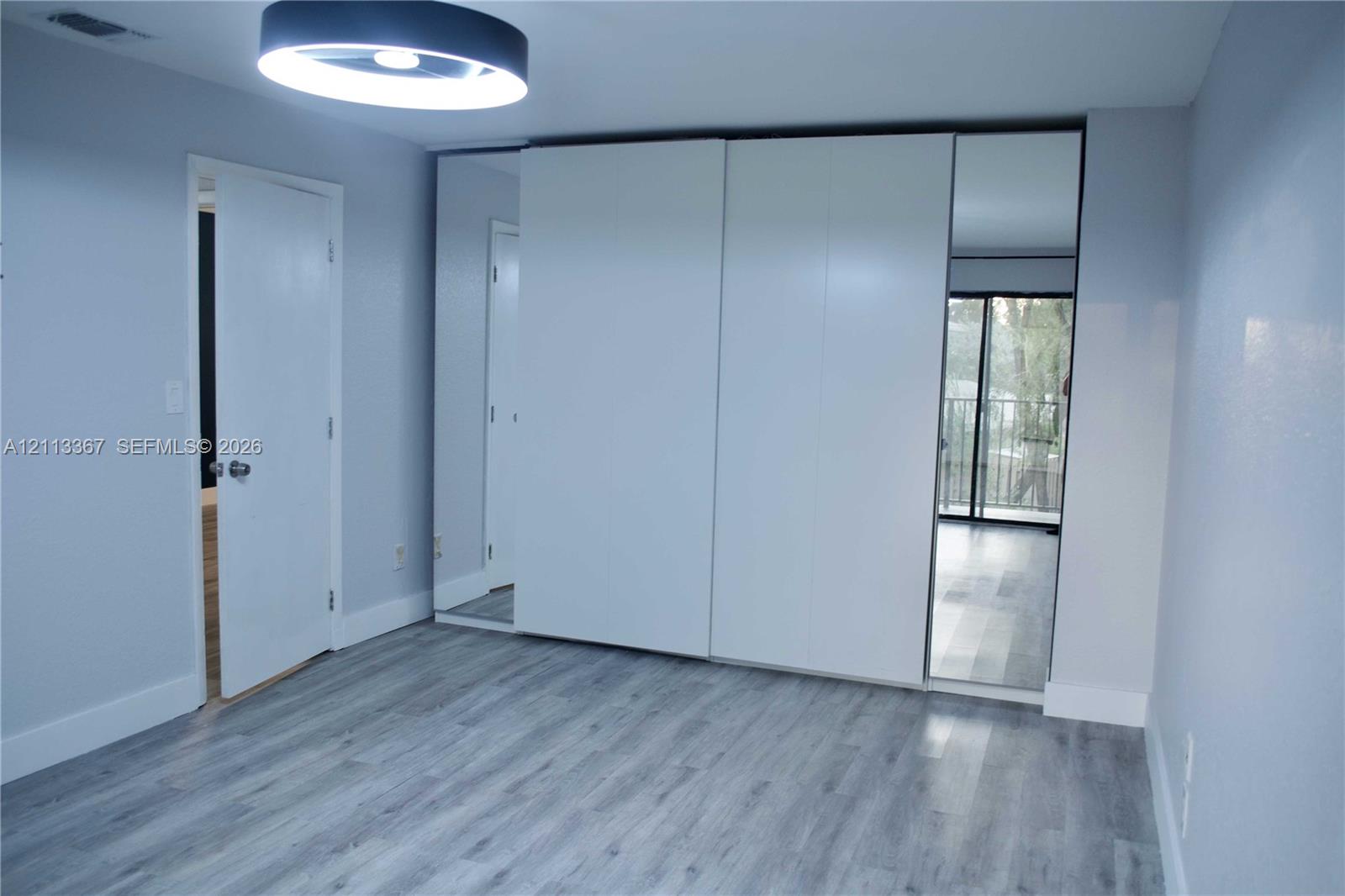 Built-in wardrobe featuring floor-to-ceiling sliding panel doors with dual mirror accents, wood-finish flooring, and a circular LED flush-mount fixture