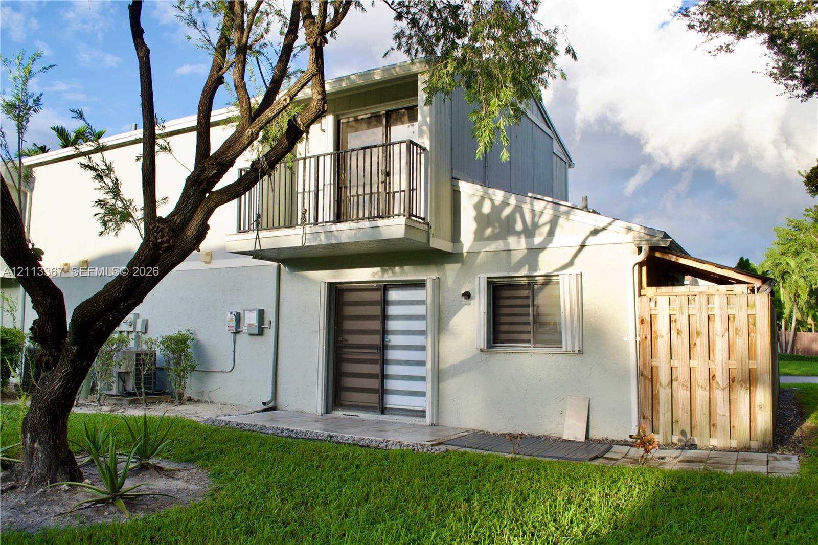 Exterior featuring a stucco facade, a second-story balcony with metal railings, sliding glass doors, and a wood-slatted privacy enclosure