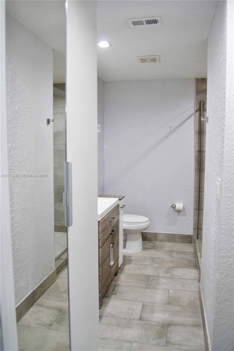 Bathroom featuring wood-finish vanity cabinetry, a rectangular sink, neutral large-format tile flooring, a glass-enclosed shower, and recessed ceiling lighting