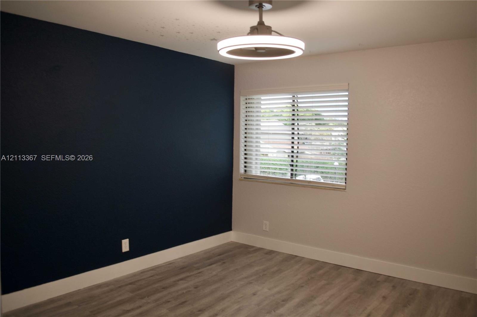 Room featuring a deep navy accent wall, wood-finish flooring, and a modern circular LED ceiling fixture