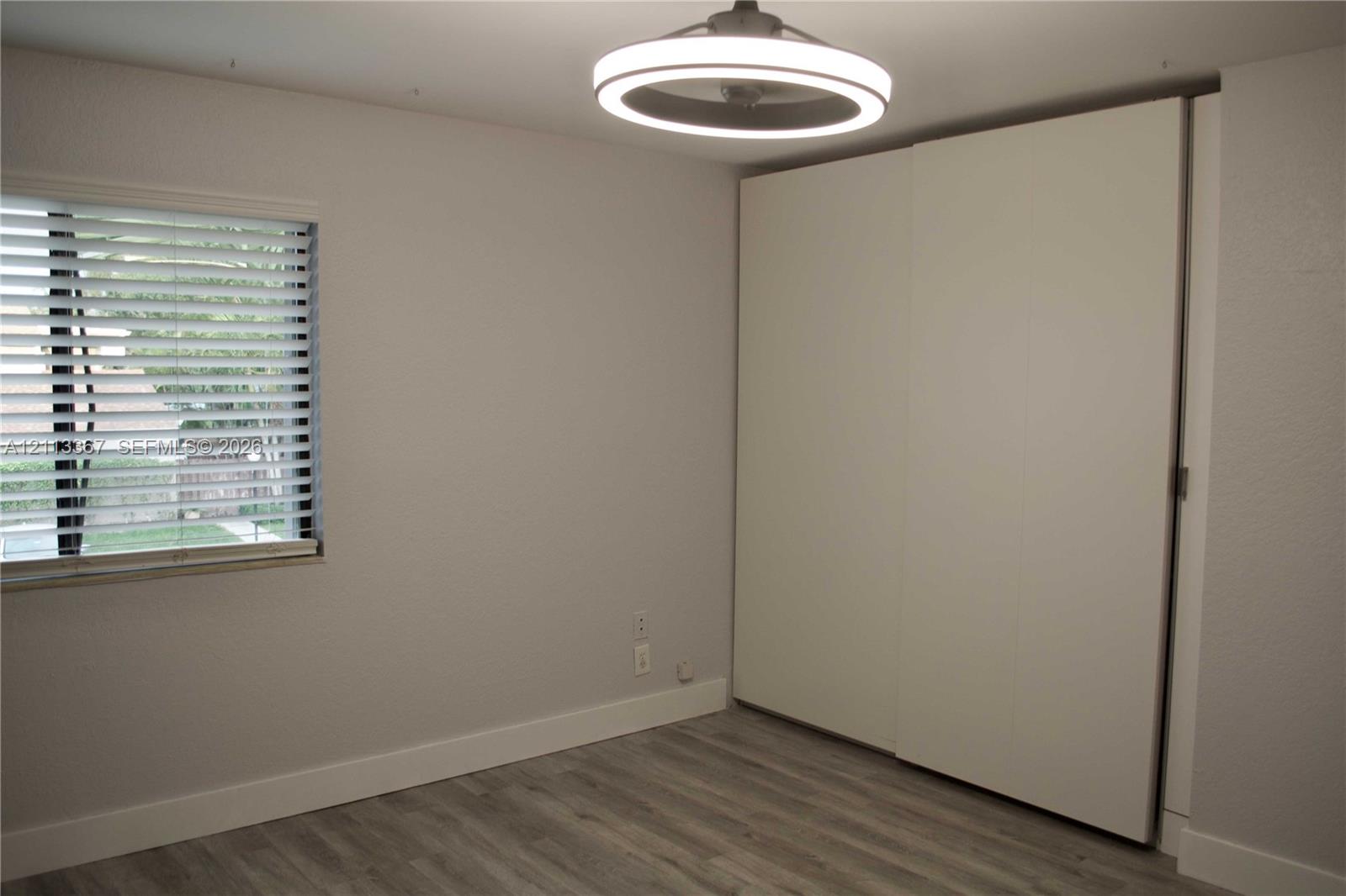 Room featuring wood-finish flooring, a wall-to-wall built-in closet with sliding doors, a horizontal-slat window blind, and a contemporary circular LED ceiling light fixture