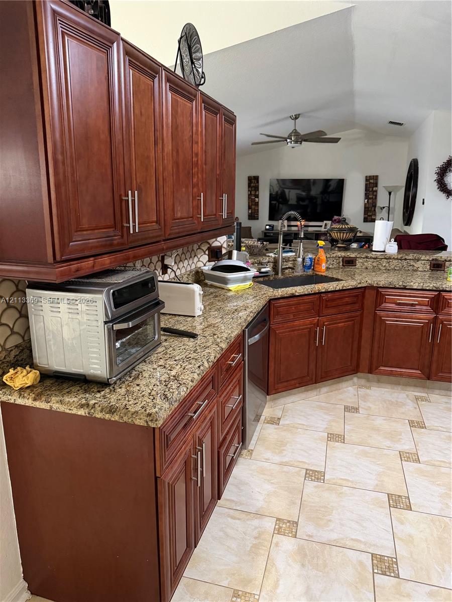 Kitchen featuring stained wood cabinetry, stone countertops, scalloped tile backsplash, integrated stainless steel appliances, and decorative tile flooring