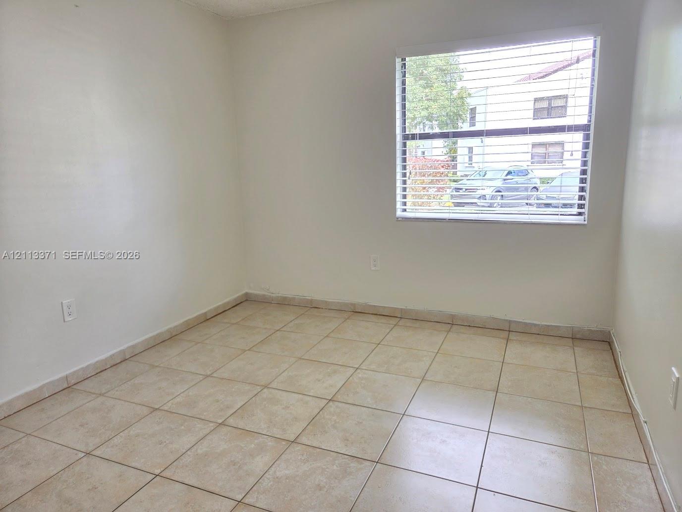 Neutral-toned ceramic tile flooring, clean painted walls, and a large window featuring horizontal blinds