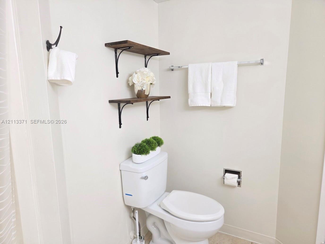Wall-mounted wood-finish shelving with decorative metal brackets, chrome towel bar, and chrome recessed toilet paper holder