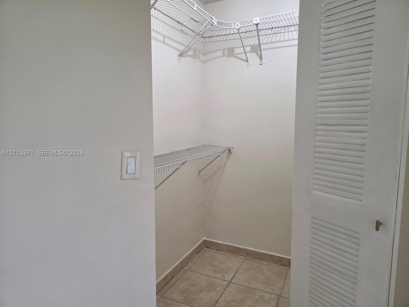 Walk-in closet featuring white louvered doors, tile flooring, and installed wire shelving