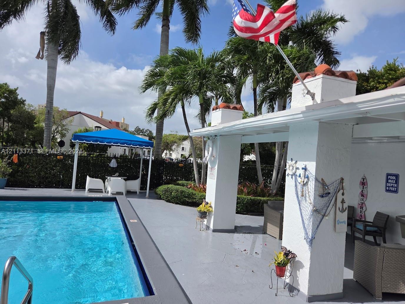 Swimming pool with concrete decking, covered patio area, and mature palm trees