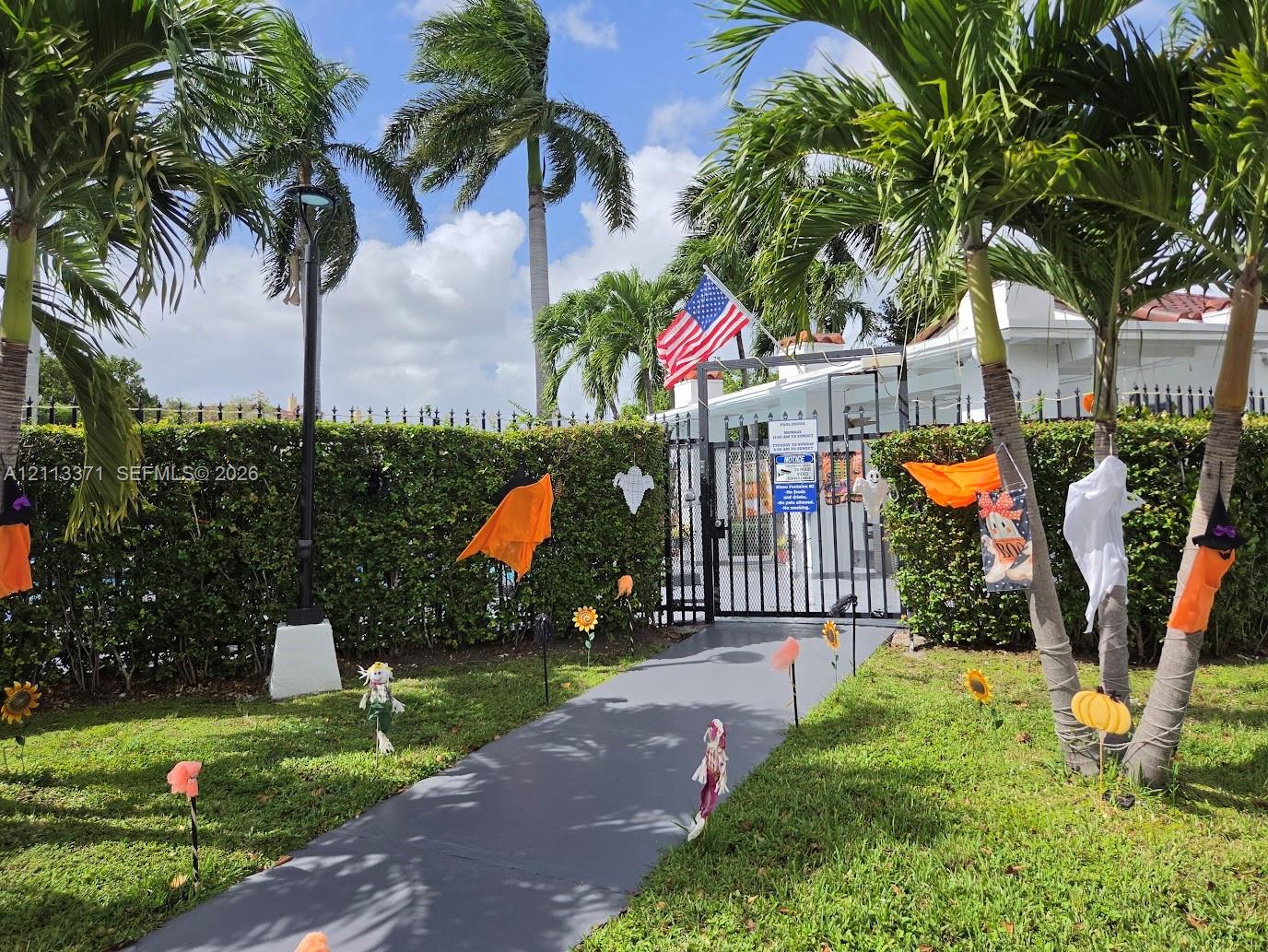 Gated entrance with a paved walkway, manicured hedging, and mature palm trees