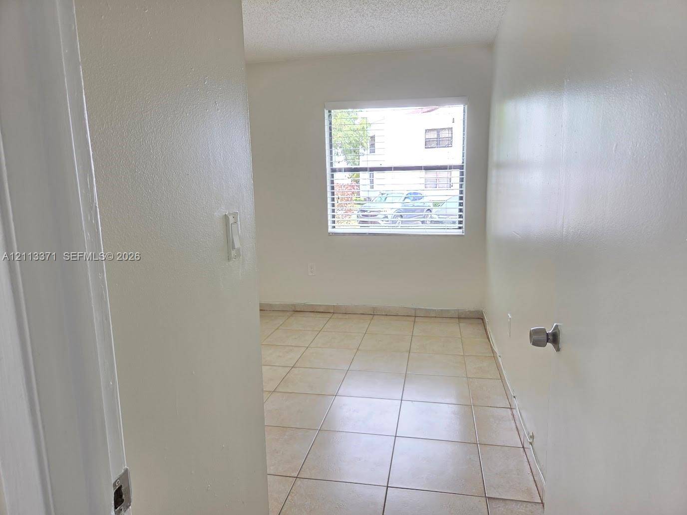 Interior space featuring neutral wall paint, large format light-toned floor tile, and a rectangular window with horizontal blinds