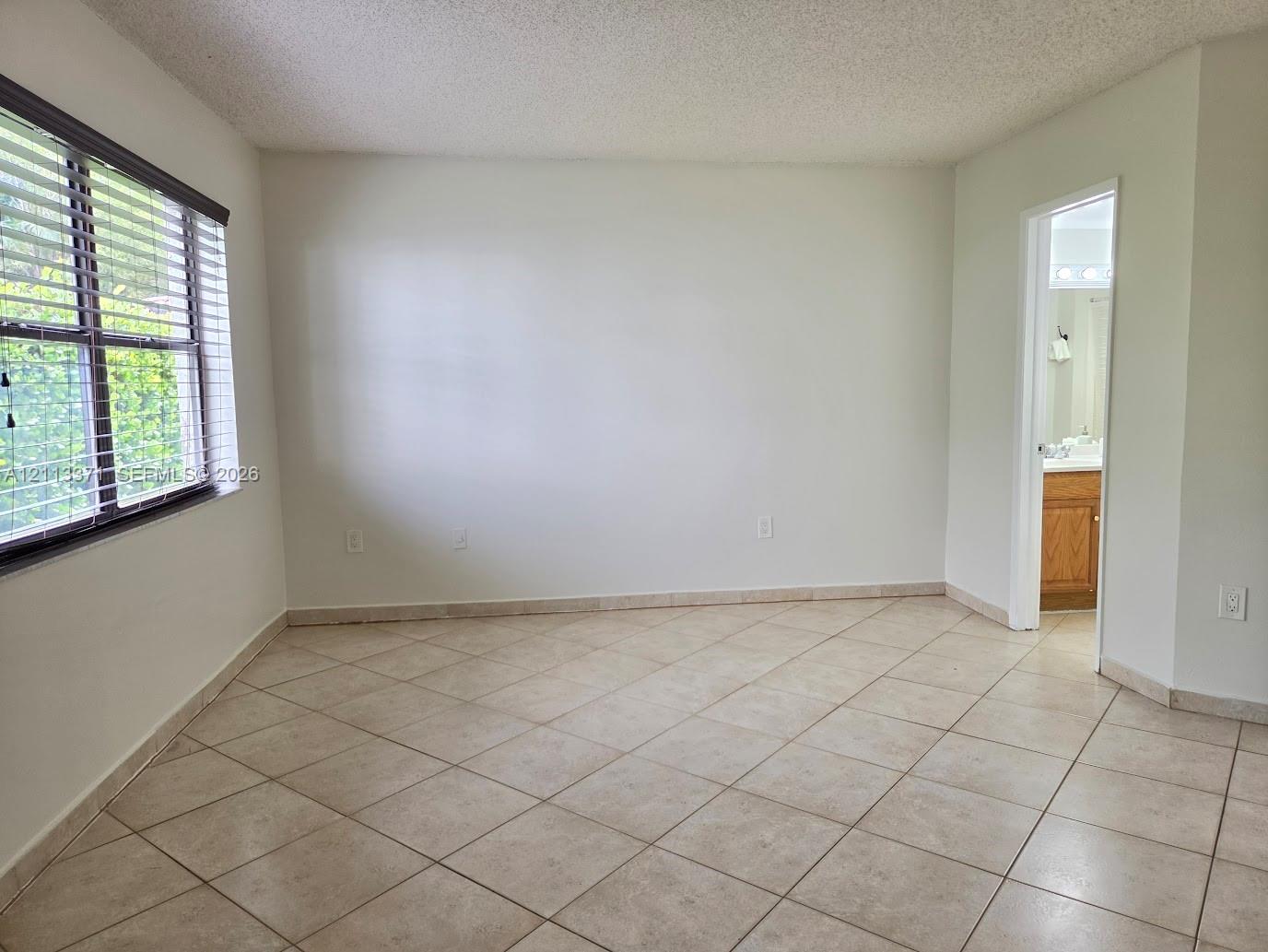 Neutral-toned tile flooring, large-format window with horizontal blinds, and smooth-finish walls