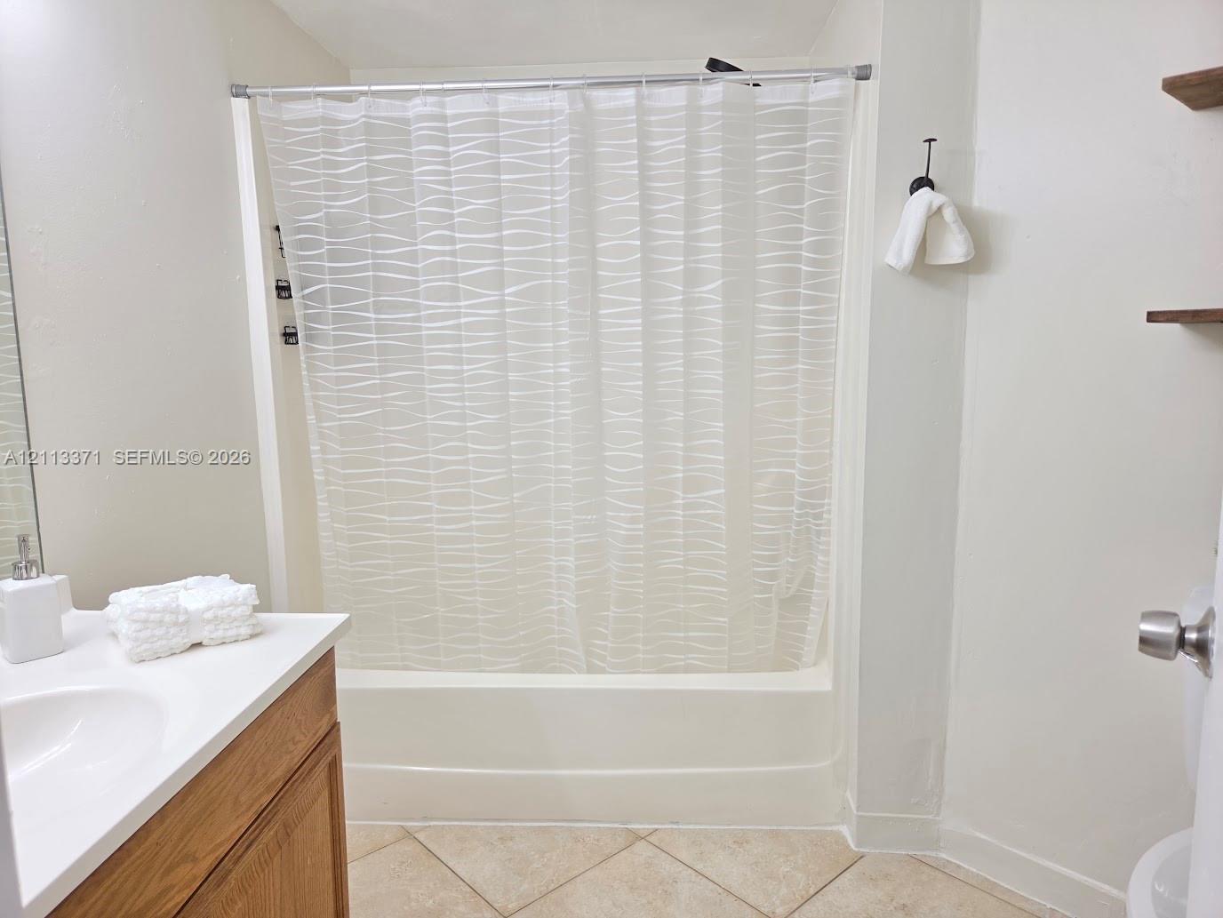 Bathroom featuring a wood-finish vanity, solid surface countertop with an integrated sink, porcelain tile flooring, and a tub-shower combination with surround