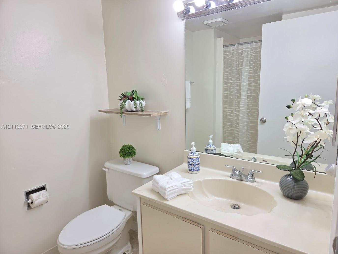 Bathroom featuring a vanity with an integrated basin, a large wall-mounted mirror, a four-light fixture, and a floating wall shelf