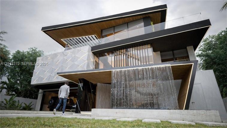 Contemporary multi-level exterior featuring a cantilevered design, geometric facade tiling, wood-finish soffits, glass balcony railings, and a built-in water feature