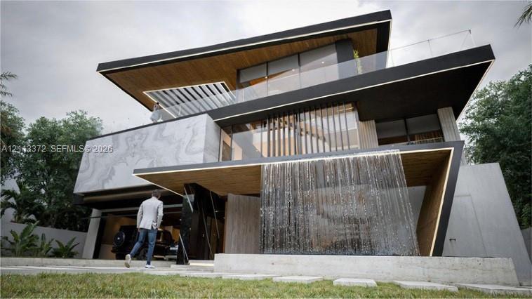 Contemporary multi-level exterior featuring architectural stone cladding, wood-finish soffits, an integrated water feature, floor-to-ceiling glass paneling, and glass-railed balconies