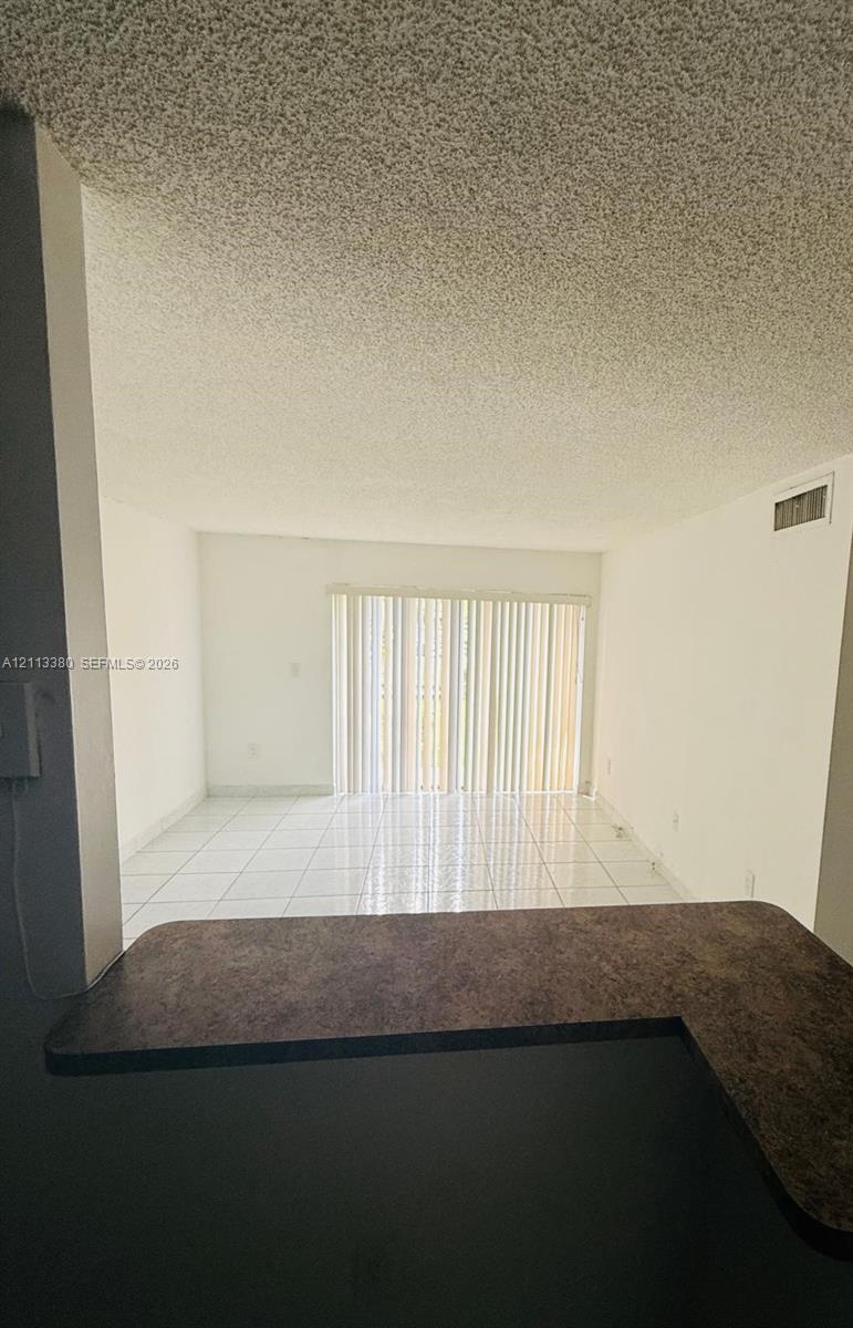 L-shaped countertop with a dark finish, white tile flooring, and vertical blinds covering a large sliding glass door