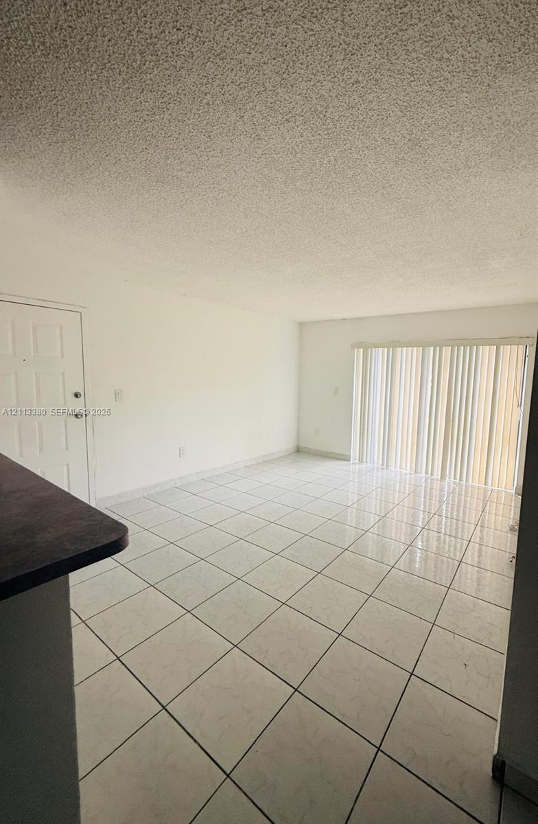 Interior space featuring large-format ceramic tile flooring, a six-panel entry door, and vertical blind window treatments