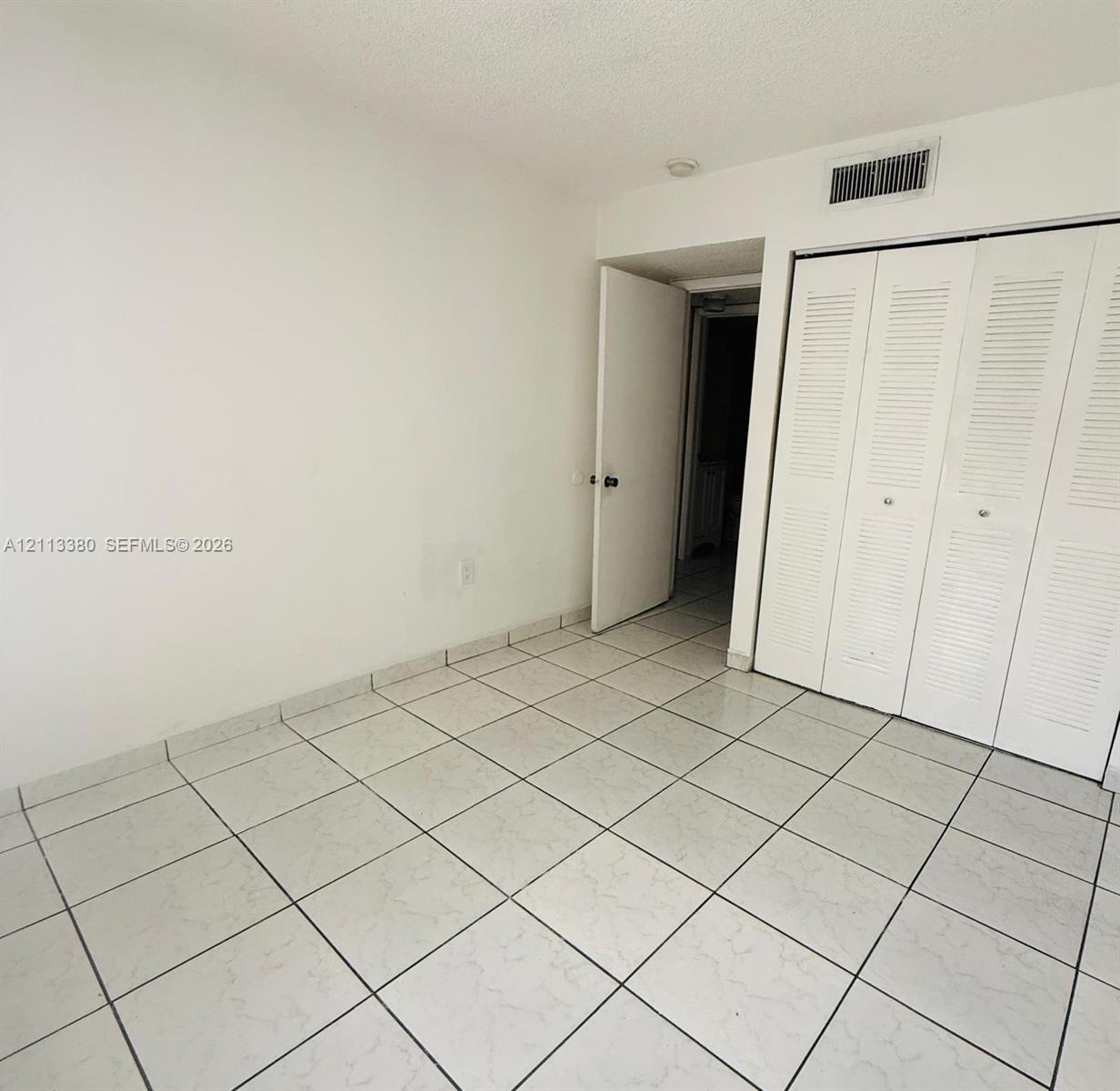 Neutral-toned ceramic floor tiling and full-height closet featuring white louvered bifold doors