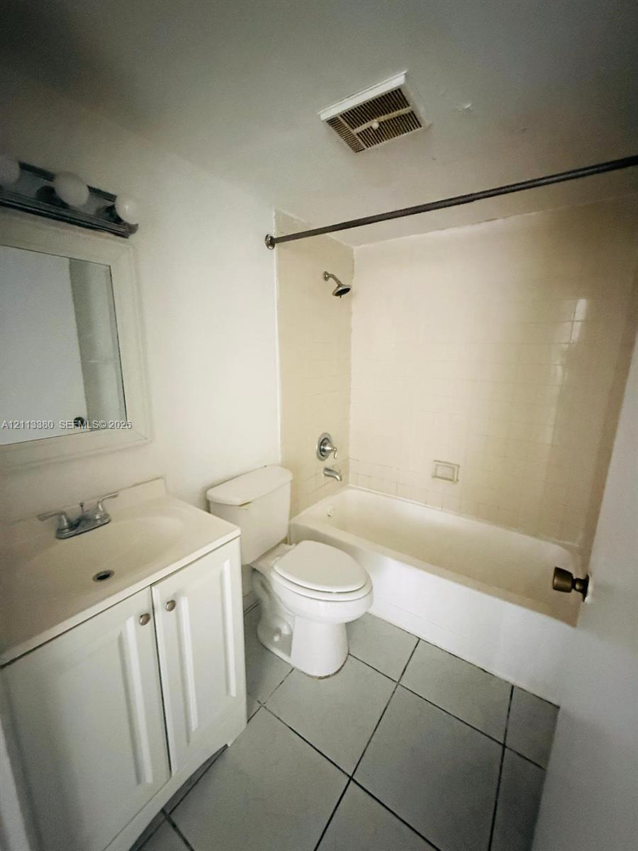 Bathroom featuring a white vanity cabinet, ceramic tile flooring, a tub and shower combination with tile surround, and a wall-mounted vanity mirror with integrated light fixture